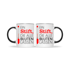 Zwei identische weiße Tassen mit schwarzem Henkel, beide bedruckt mit rotem Kuli und Spruch „Ein Stift, die alle bluten lassen“ – Geschenkset für Lehrer.